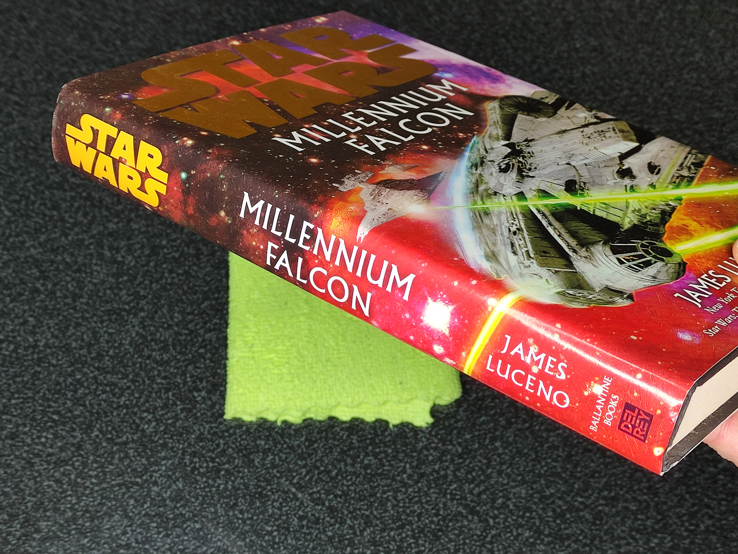 Book titled 'Millennium Falcon' by James Luceno on a dark surface with a green cloth underneath.