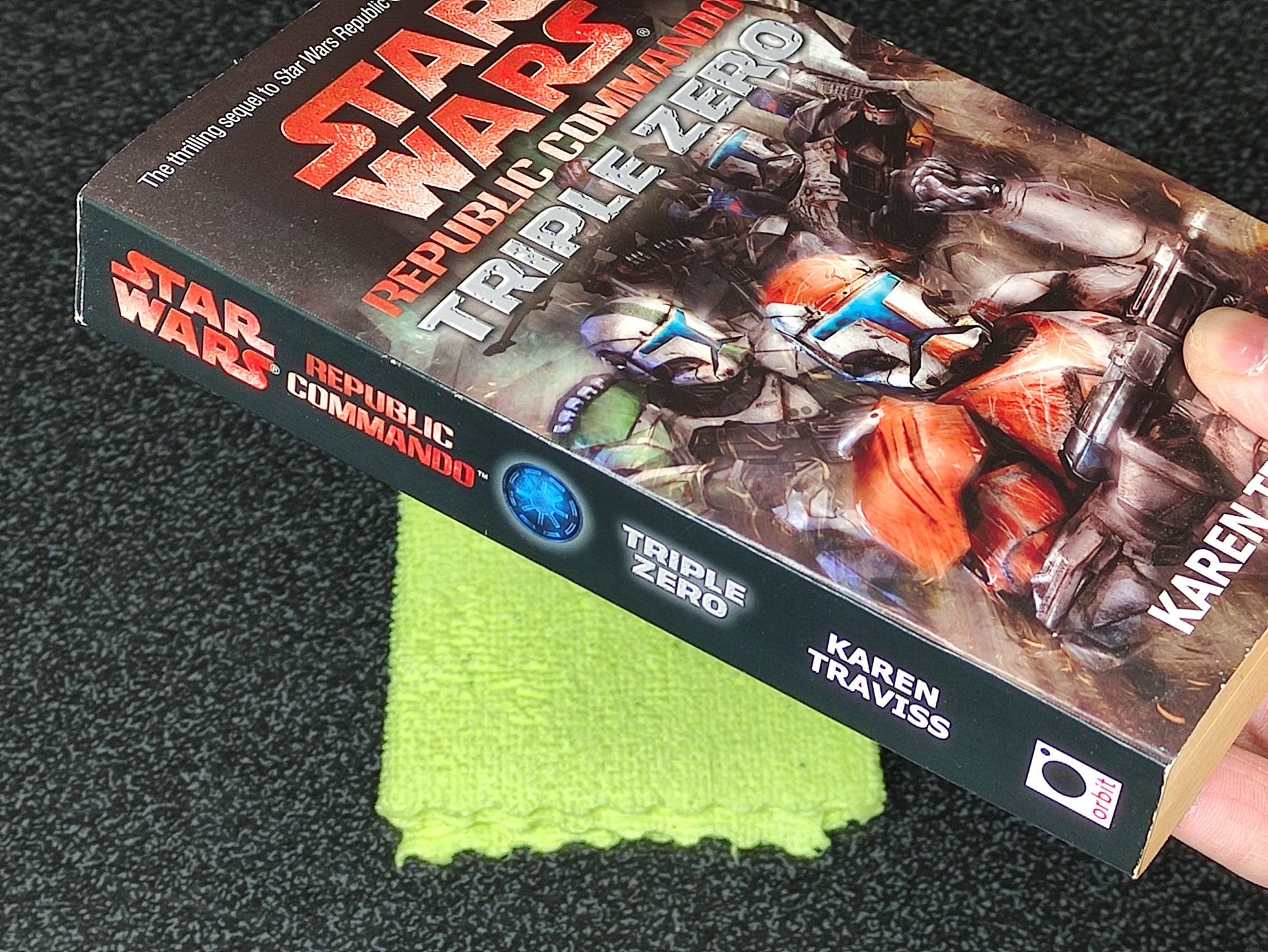 Book titled 'Star Wars: Republic Commando Triple Zero' held by a hand on a dark surface with a green cloth underneath.