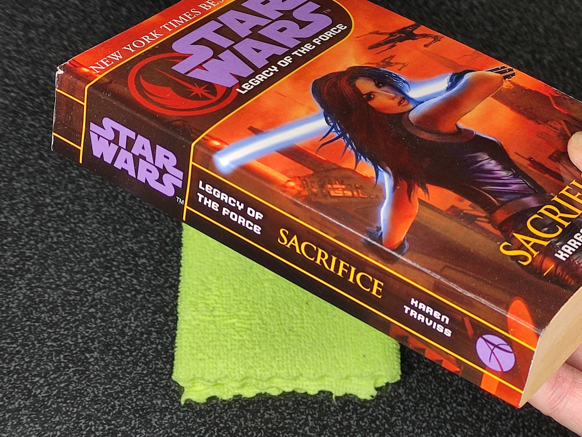Star Wars book titled 'Sacrifice' with a character holding a lightsaber on the cover, held by a hand.