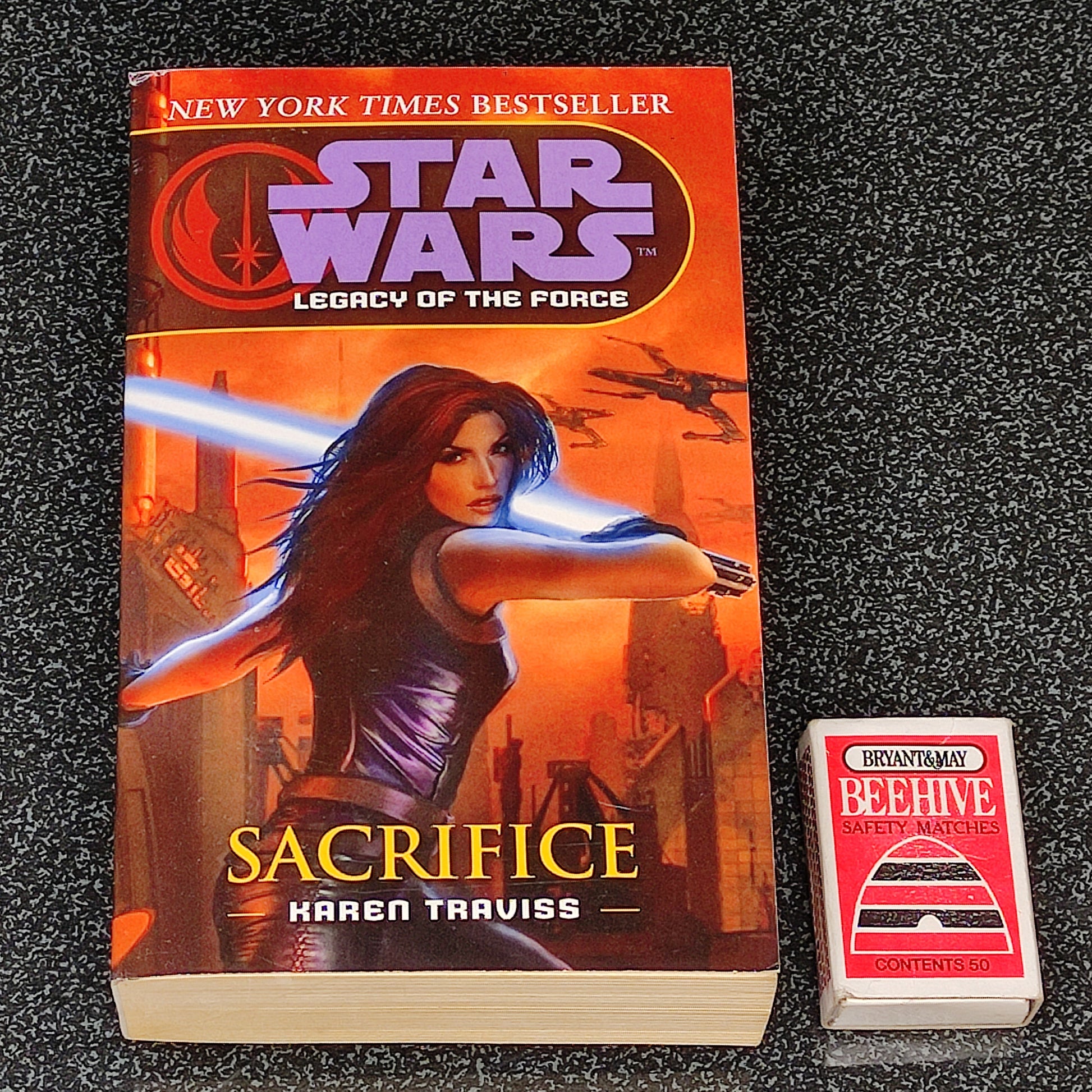 Book titled 'Sacrifice' by Karen Traviss from 'Star Wars: Legacy of the Force' series on a dark textured background.