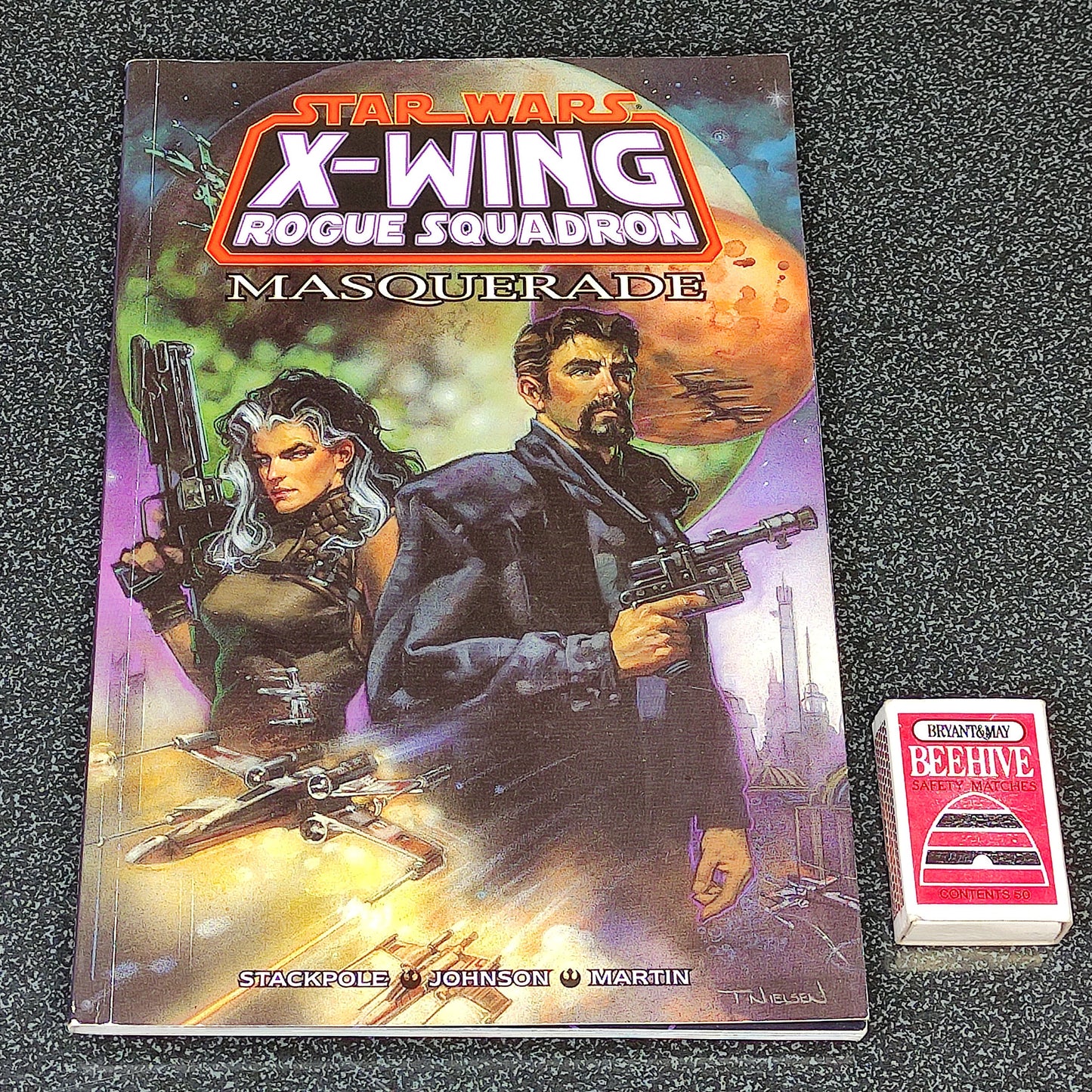 Star Wars X-Wing Rogue Squadron Masquerade book with a small card on a dark textured surface