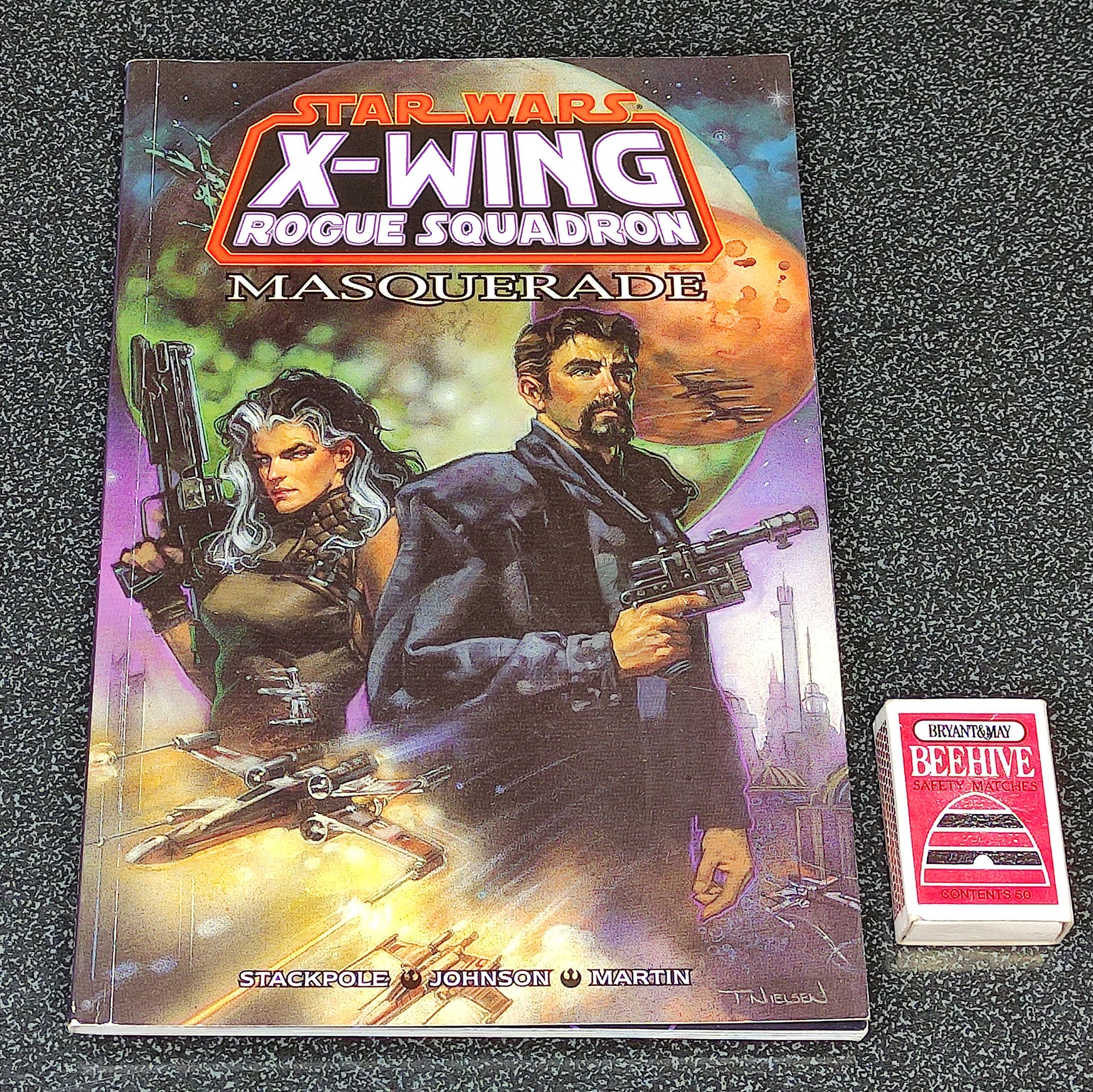 Star Wars X-Wing Rogue Squadron Masquerade book with a small card on a dark textured surface