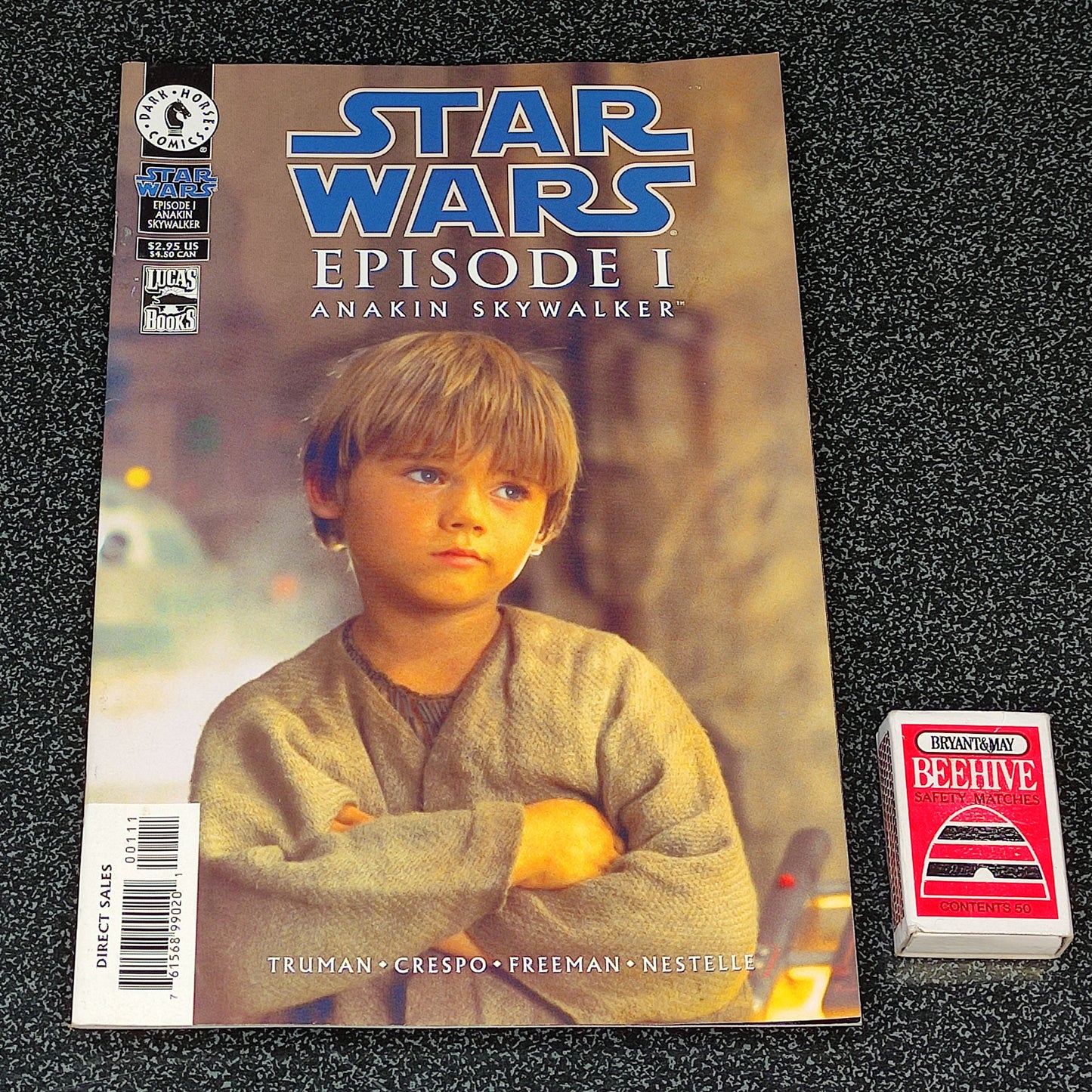Comic book titled 'Star Wars Episode I: Anakin Skywalker' on a textured black surface with a small card beside it.