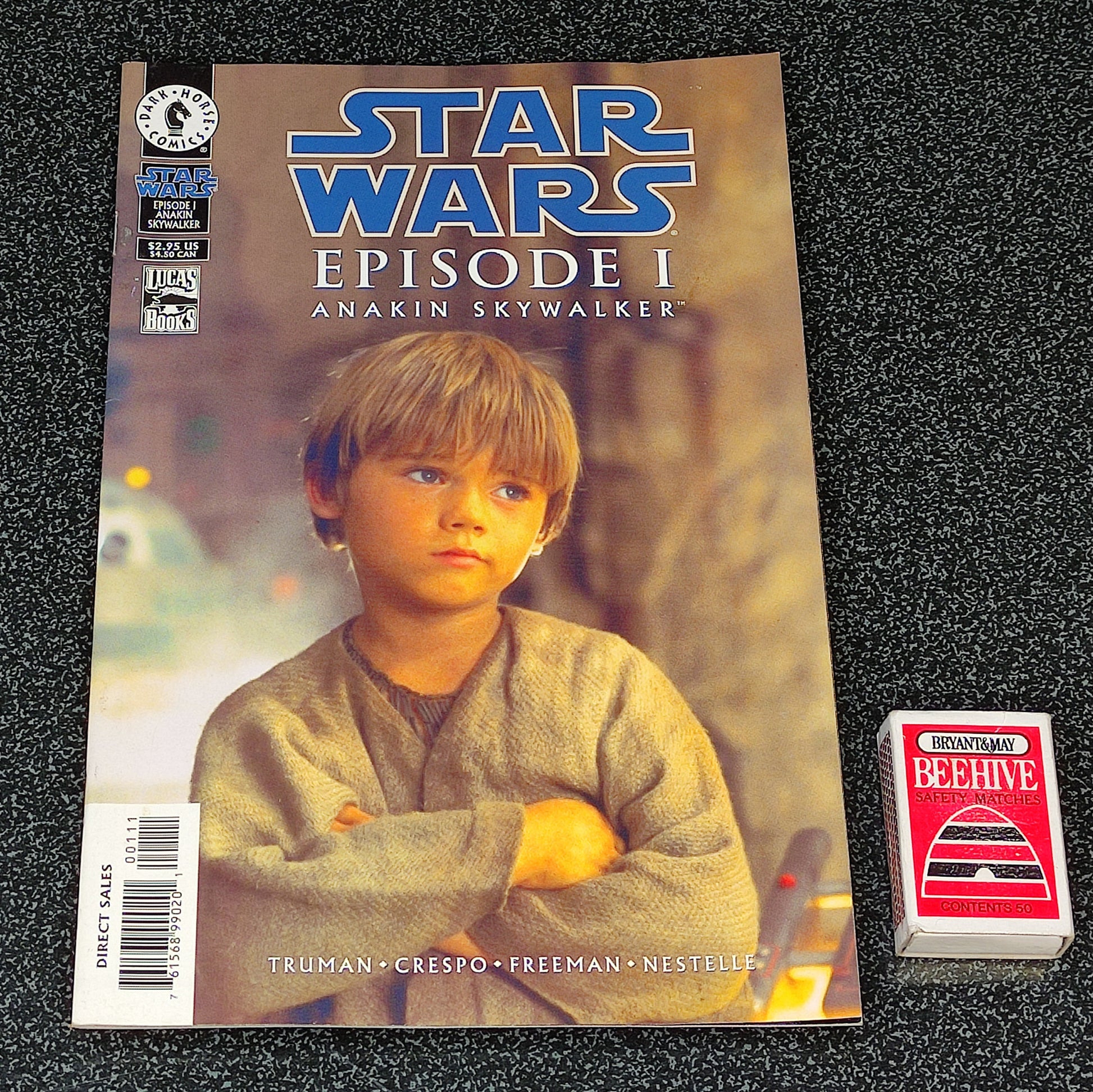 Comic book titled 'Star Wars Episode I: Anakin Skywalker' on a textured black surface with a small card beside it.