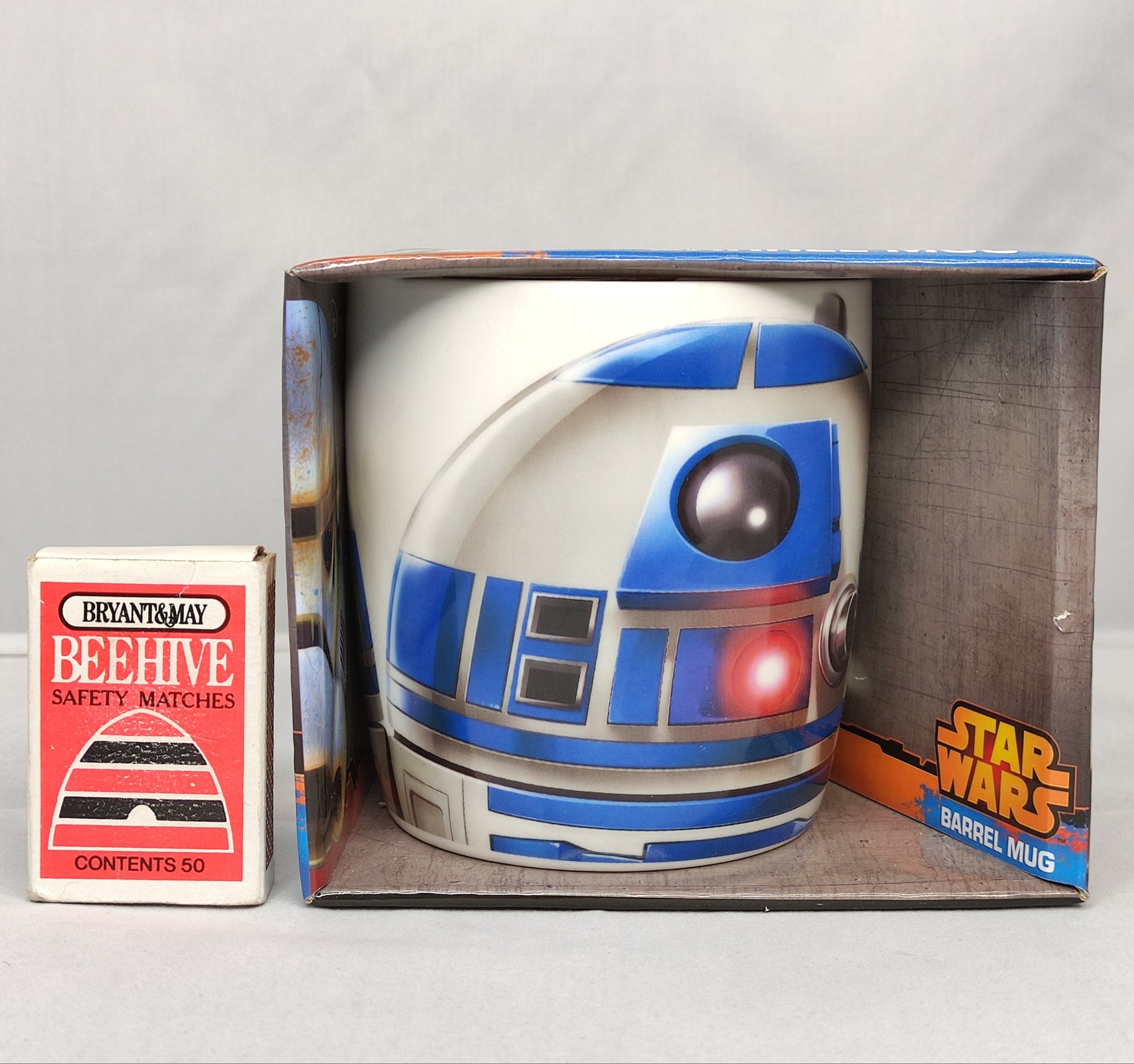 Star Wars R2-D2 mug in packaging with a matchbox on a gray background