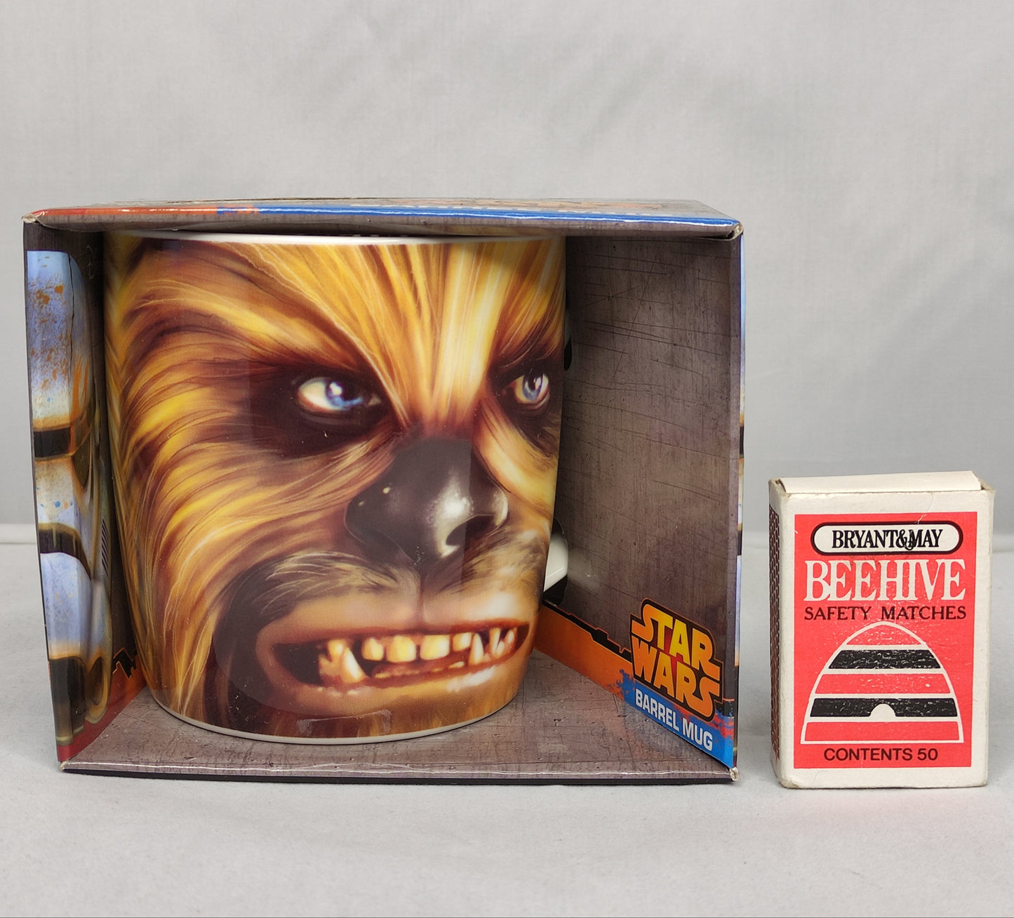 Star Wars-themed mug with Chewbacca design in packaging next to a box of matches on a gray background