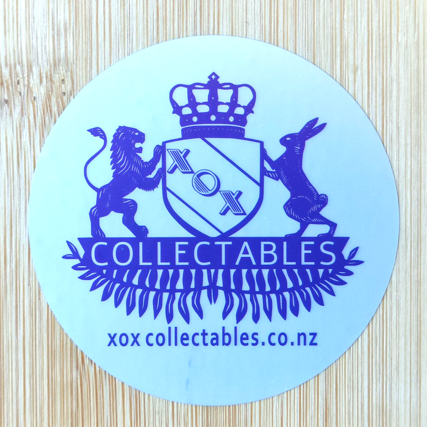XOX Collectables Coat of Arms Sticker. Purple on reflective matte silver on a wooden surface