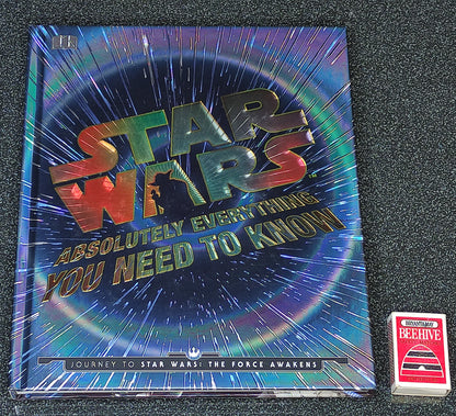Star Wars book titled 'Absolutely Everything You Need to Know' on a dark textured surface with a deck of cards.