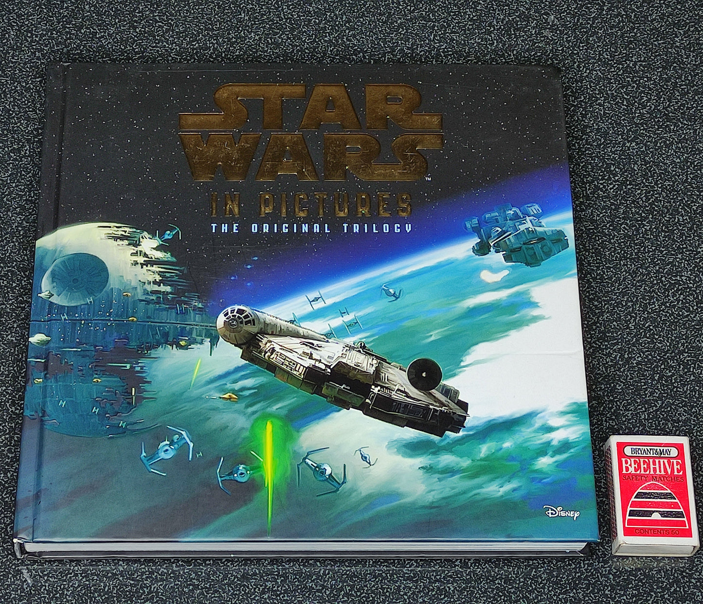 Star Wars book titled 'In Pictures: The Original Trilogy' on a textured surface with a deck of cards.