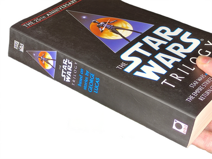 Book titled 'The Star Wars Trilogy' held by a hand on a white background