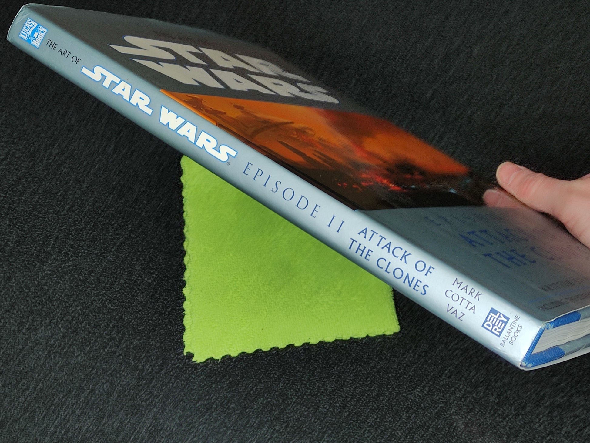 Book titled 'The Art of Star Wars Episode II: Attack of the Clones' held by a hand on a dark surface with a green cloth.