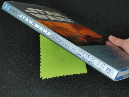 Book titled 'The Art of Star Wars Episode II: Attack of the Clones' held by a hand on a dark surface with a green cloth.