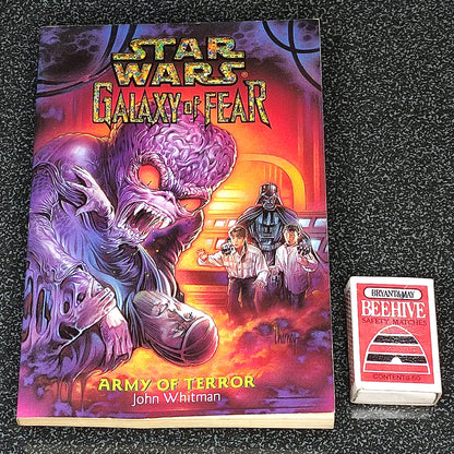 Book titled 'Star Wars: Galaxy of Fear Army of Terror' by John Whitman on a dark textured surface with a deck of cards.