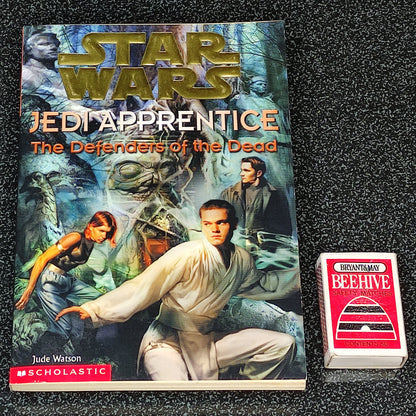 Book titled 'Jedi Apprentice: The Defenders of the Dead' by Scholastic on a dark textured background