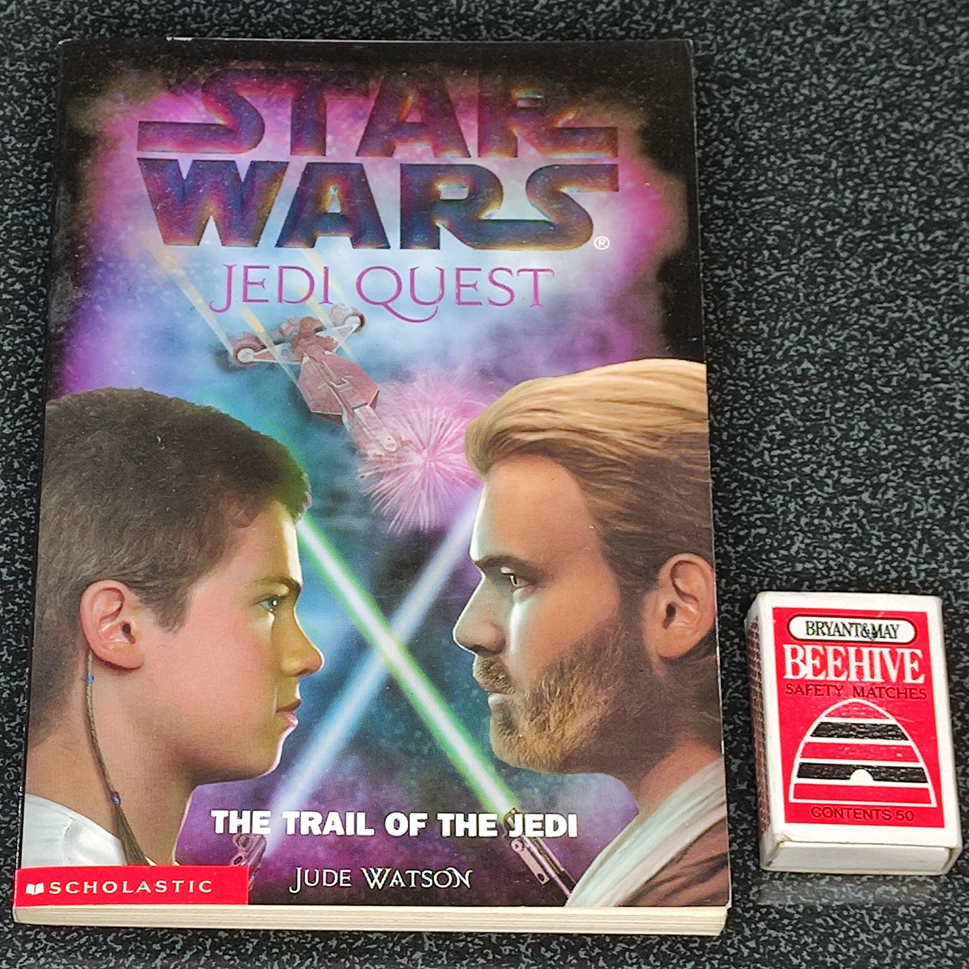 Book titled 'Star Wars Jedi Quest: The Trail of the Jedi' by Jude Watson on a dark textured surface with a small box labeled 'Beehive'.