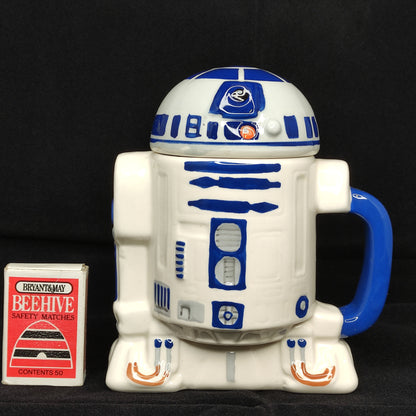 R2-D2 mug from Star Wars with a small box labeled 'Beehive' on a black background
