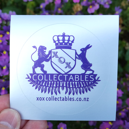 XOX Collectables Coat of Arms Sticker. Purple on reflective matte silver. In front of purple flowers